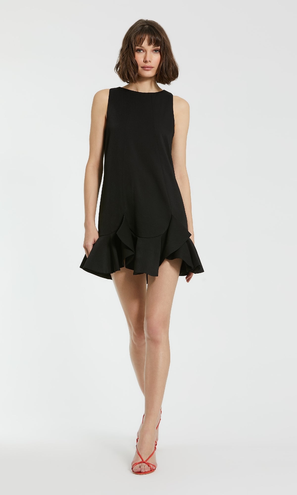 A woman wearing the Mac Duggal 20957 black cocktail party dress with a ruffled hem and red strappy heels poses against a plain white background.